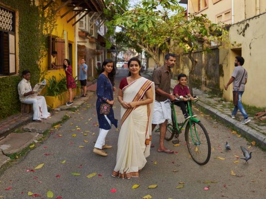 Woman in a street and a man on a bicycle with his child for Kerala Tourism Campaign by Joey L. 