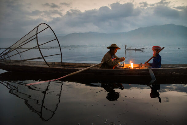 Two fisherman sit by a campfire in a canoe on the inle lake