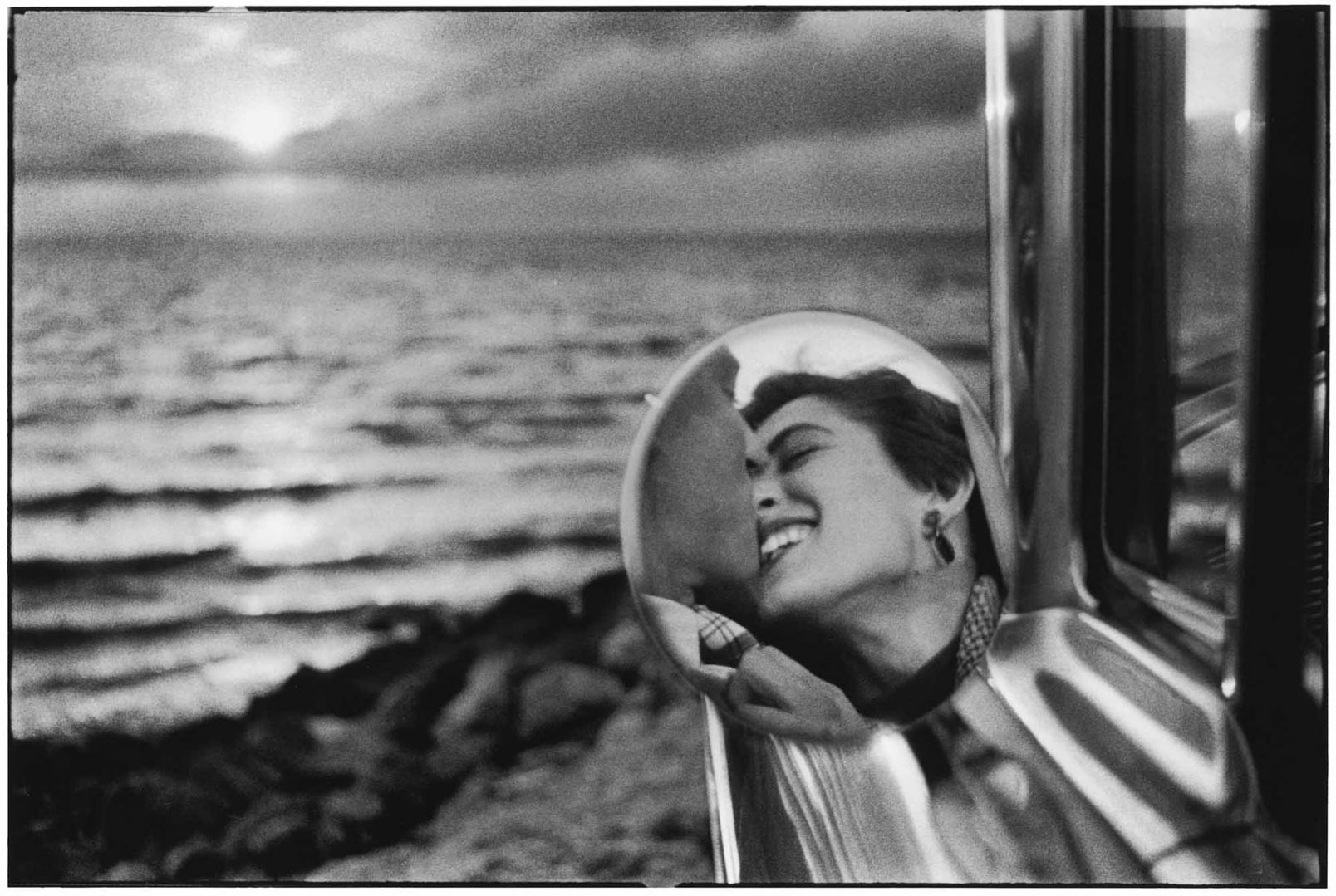 a reflection in a rear view of a man and a woman kissing at the beach 