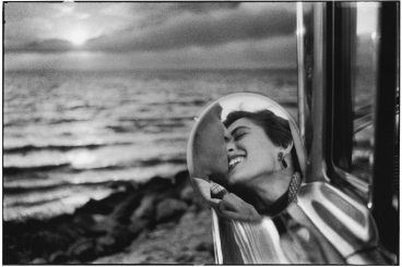 a reflection in a rear view of a man and a woman kissing at the beach 