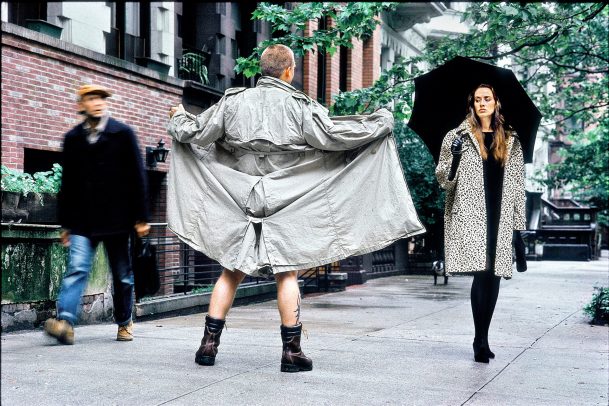 man with open coat in front of a not impressed woman holding a black umbrella