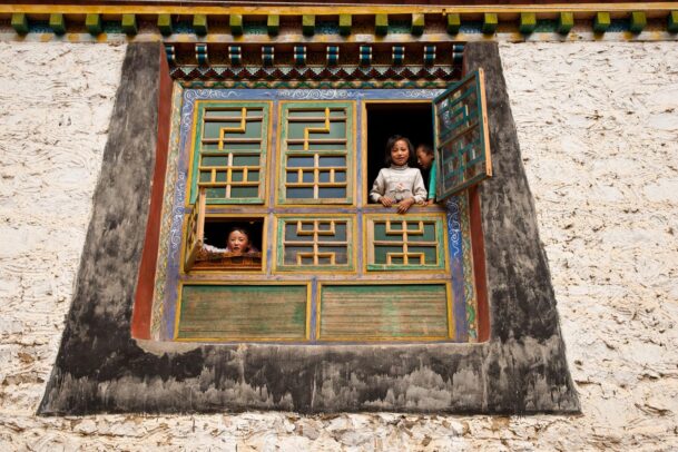 Children from intricately decorated windows, framed by traditional Tibetan architecture